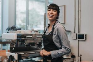 mujer feliz dueña del café de pie detrás del mostrador de una cafetería. barista femenina de pie detrás del mostrador en la cafetería. concepto de propietario de negocio. foto