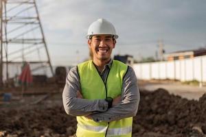 hombre ingeniero trabajando en el sitio de construcción. hombre trabajador asiático sonriendo y cruzado de brazos en el sitio de construcción. foto