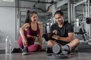 ejercicio de mujer asiática con entrenador personal en el gimnasio. entrenador personal que muestra y habla sobre el plan de ejercicio con una mujer sana. foto