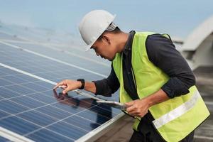 hombre ingeniero comprobando la energía de los paneles solares con tableta. revisión técnica y servicios de paneles solares fotovoltaicos. concepto de energía sostenible. foto