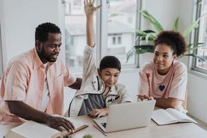 Asian boy learning online class from home with family. little boy sit with sister and dad using laptop learning online education from home. photo