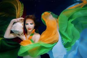 Redhead woman with big sea shell in colorful clothes on the dark background underwater photo