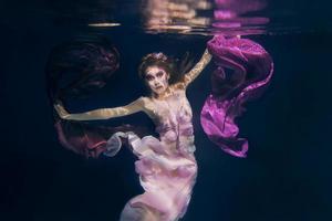 woman in colorful clothes on the dark background swimming underwater photo