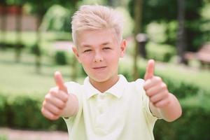 portrait of cute handsome blonde eleven old boy with thumb up outdoor. Good sign and ok concept