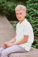 retrato de un lindo y apuesto niño rubio de once años sentado al aire libre en el parque. crecimiento, infancia, concepto de separación. foto