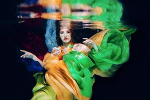 Redhead woman in colorful clothes on the dark background, underwater photo