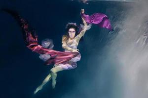 woman in colorful clothes on the dark background swimming underwater photo