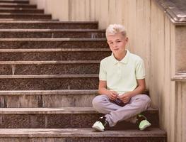 portrait of cute handsome blonde eleven old boy sitting on the stairs outdoor. Growing up, childhood, separating concept photo