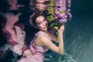 woman with lilac bouquet in colorful clothes on the dark background swimming underwater photo
