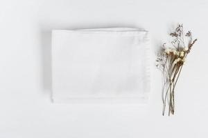 Stack of fabrics with dry flowers over light background. Flat lay with white folded linen cloth for mock up. photo