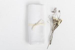 Linen napkin tied with ribbon on white table. Fabric and dried flowers in rustic style for mock up. photo