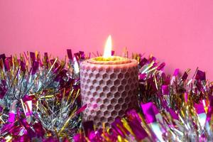 Burning wax candle with tinsel around. Pink color photo