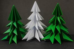 dos árboles de navidad verdes de origami y uno blanco sobre fondo negro. foto