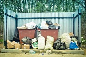 Fenced waste bins filled with garbage. Garbage lies next to the bins. Dump photo