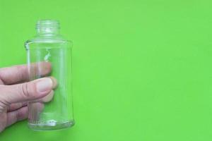 Transparent glass empty bottle in hand on a green background with place for your design. photo