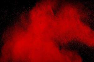 abstract red dust splattered on black background. Red powder explosion.Freeze motion of red particles splashing. photo