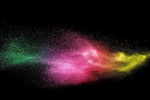 Green pink and yellow dust particles explosion on black background. Color powder dust splash. photo
