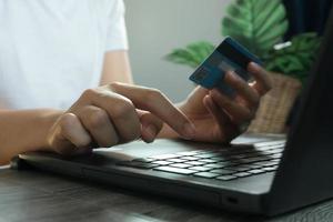 manos sosteniendo la tarjeta de crédito y usando la computadora portátil. las compras en línea. trabajo desde el concepto de casa foto