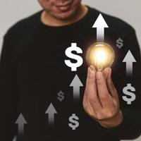 Hand holding a light bulb rises up with investment arrow for business growth and profit increase concept. photo