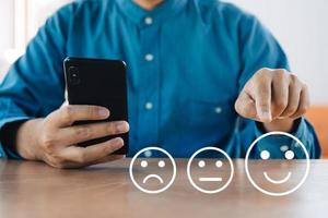 el hombre de negocios usa un teléfono inteligente dando calificación con un icono feliz, concepto de encuesta de satisfacción del cliente foto