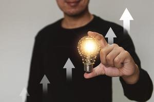 Hand holding a light bulb rises up with investment arrow for business growth and profit increase concept. photo