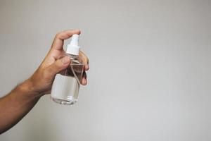 Handsome man holding alcohol spray bottle for hygiene cleaner coronavirus on grey background. photo