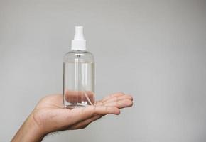 Handsome man holding alcohol spray bottle for hygiene cleaner coronavirus on grey background. photo