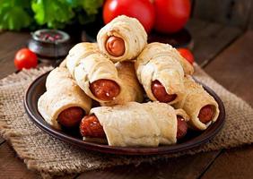 Sausage in the dough sprinkled with sesame seeds on a wooden background in rustic style photo