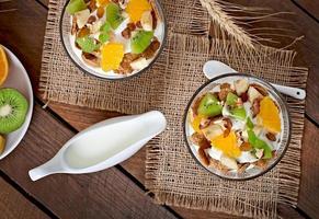 Healthy dessert with muesli and fruit in a glass bowl on the table photo