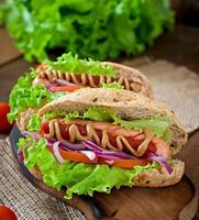 Perrito caliente con salsa de tomate mostaza y lechuga sobre fondo de madera. foto