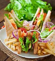 Club sandwich with cheese, cucumber, tomato, smoked meat and salami. Served with French fries. photo