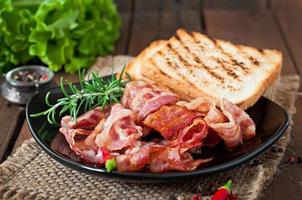 Fried bacon and toast on a black plate on a wooden background photo