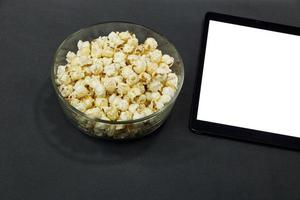 Glass cup with salted popcorn digital tablet in a gray armchair. photo