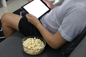 taza de vidrio con tableta digital de palomitas de maíz saladas en un sillón gris. foto