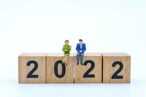 2020 New Year Planning concept. Closeup of businessman and businesswoman miniature figure sitting and talking on stack of wooden number block isolated on white background. photo
