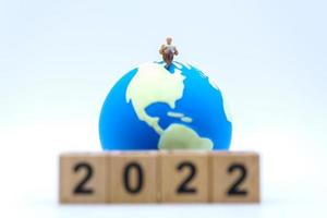 2022 New Year and Business Concept. Closeup of businessman miniature figures sitting and reading a book or newspaper on mini world ball on white background with wooden number block. photo