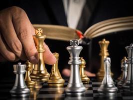 Hand of businessman moving the golden king chess to fighting silver king chess with opening book guideline play successfully in the competition. management or leadership strategy and teamwork concept. photo