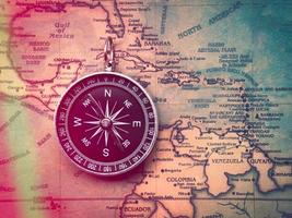 The compass is placed on the ancient or vintage world map between the United States of America and South America. Travel geography navigation concept background. photo