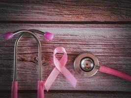 cinta rosa y estetoscopio en estilo vintage de mesa de madera. símbolo de cáncer de mama, concepto de atención médica foto