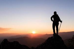 Silhouette of hiker standing on top of hill and enjoying sunrise over the valley.   Ambition and success concept photo