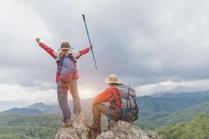 los escaladores activos disfrutan del paisaje. mochileros masculinos y femeninos con mochilas y muletas en la cima de una montaña. foto