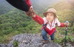 Young couple traveling, Helping hand, hiker woman getting help on hike smiling happy overcoming obstacle, Tourist backpackers walking in  forest. photo