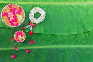 Songkran Festival background with jasmine garland Flowers in a bowl of water, perfume and limestone on a green wet banana leaf background. photo