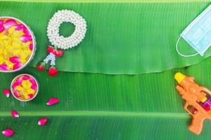 fondo del festival songkran con flores de guirnalda de jazmín en un tazón de agua, perfume y piedra caliza sobre un fondo verde de hoja de plátano húmedo. foto