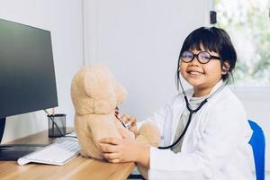 un niño vestido de médico se sienta y examina un oso de peluche en el hospital. foto