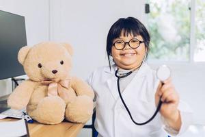 un niño vestido de médico se sienta y examina un oso de peluche en el hospital. foto