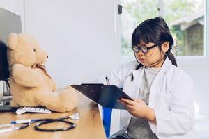 un niño vestido de médico se sienta y examina un oso de peluche en el hospital. foto