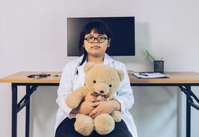 A child dressed as a doctor sits and examines a teddy bear in the hospital. photo