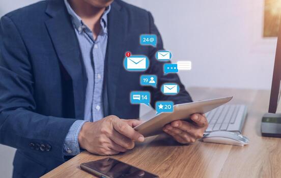 A businessman sits in front of a computer using a tablet to send text messages. photo