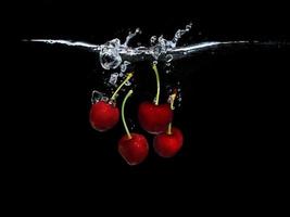 Red sweet cherries under water isolated on black background photo